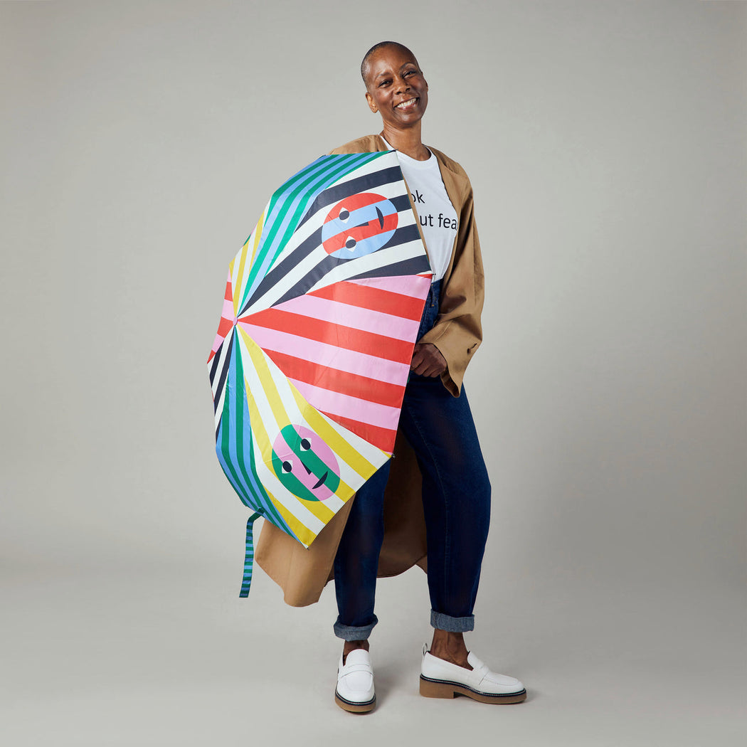 Female model holding multi-color striped umbrella with smiley face graphics down by her side