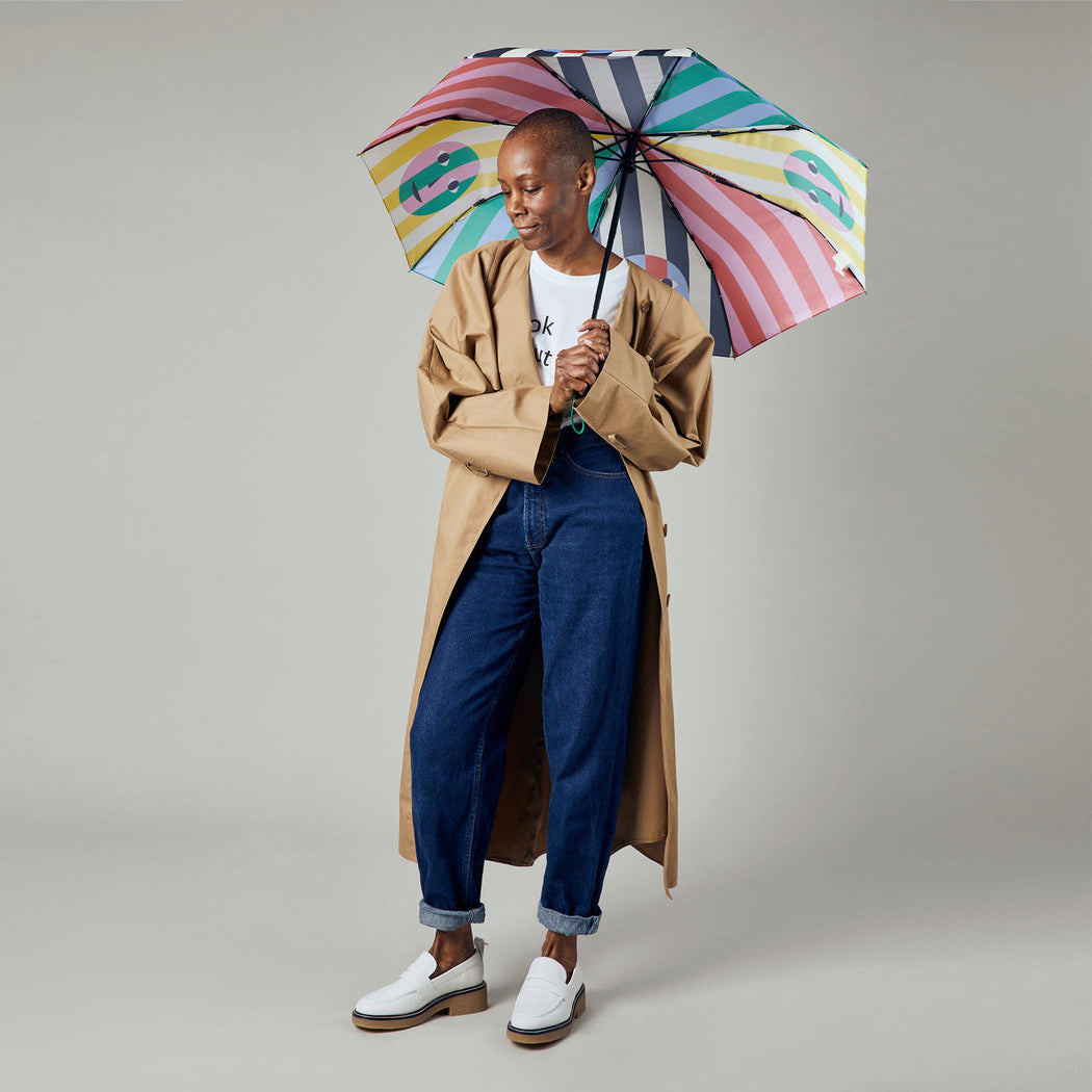 Female model holding multi-color striped umbrella with smiley face graphics over her head