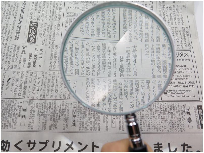 Small magnifying glass with black PVC handle being held over a newspaper