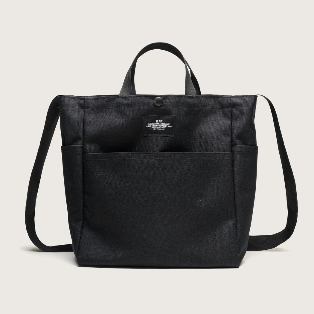 Black canvas tote with 4 exterior pockets, snap closure, handles & shoulder strap, front view