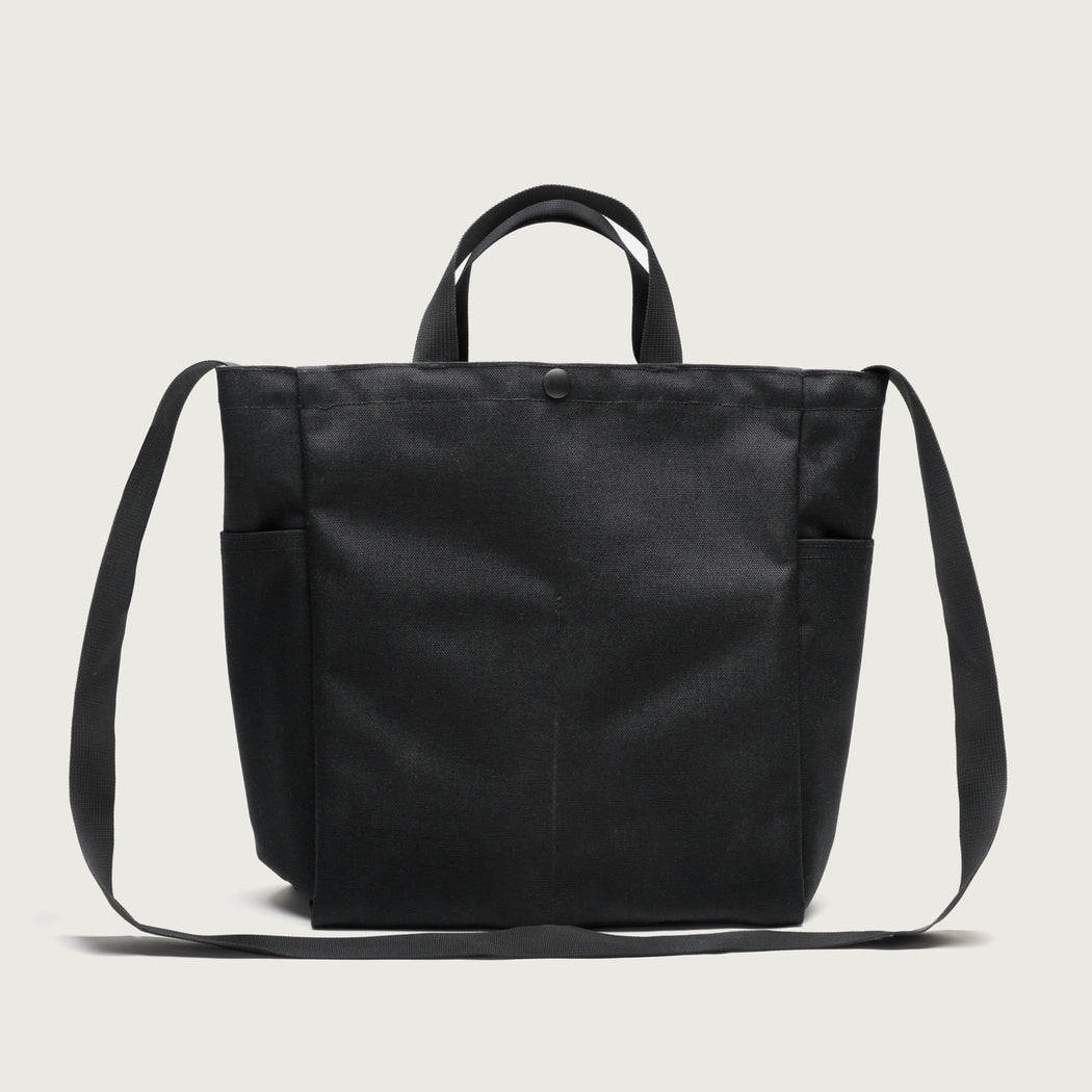 Black canvas tote with 4 exterior pockets, snap closure, handles & shoulder strap, back view