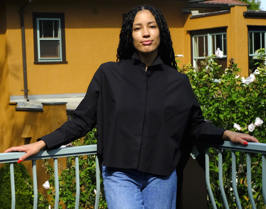 female model wearing black long sleeve shirt with pleated front bib, wing collar, hidden buttons & curved hem