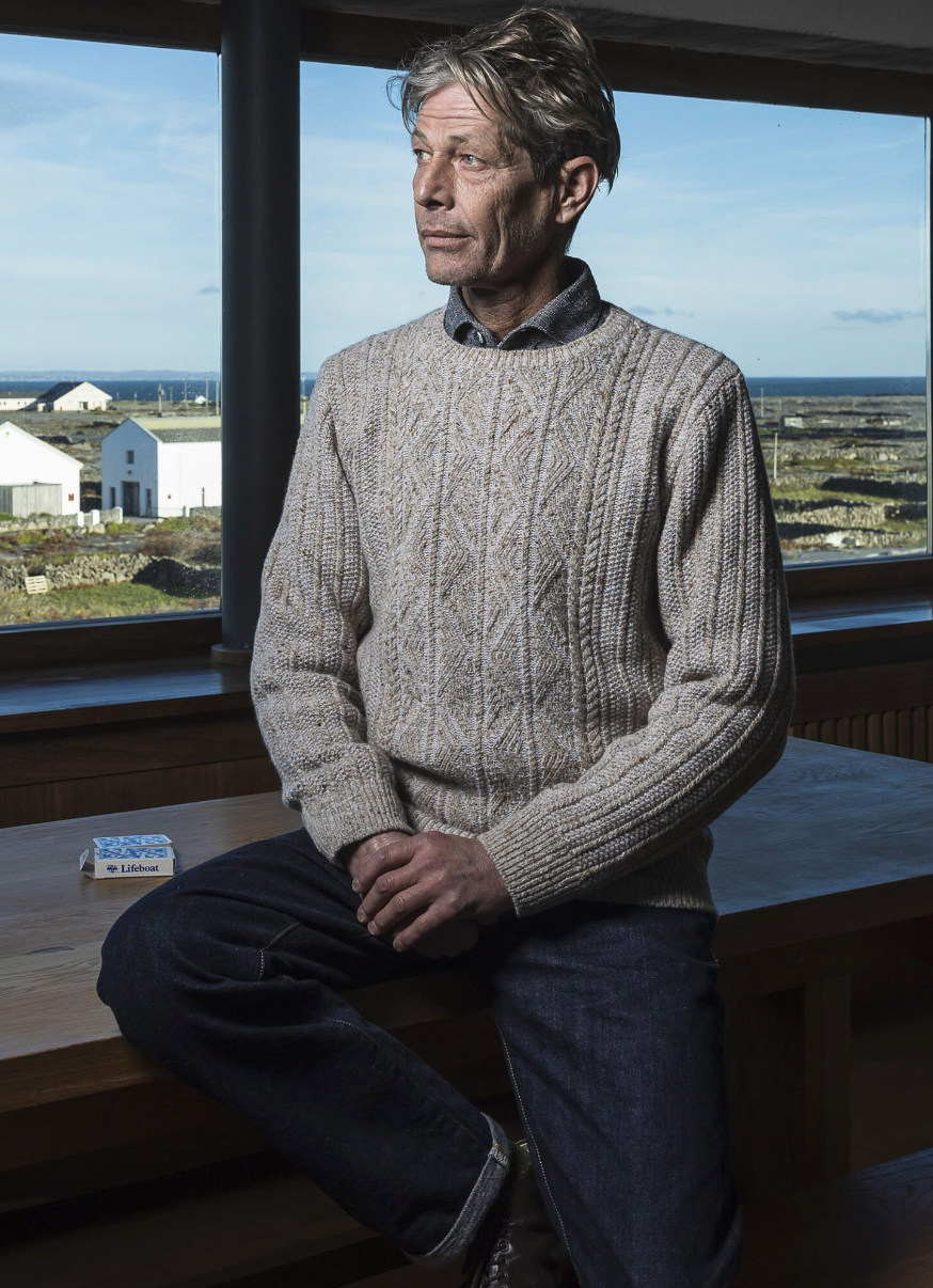 Male model wearing light tan cable knit sweater and blue jeans