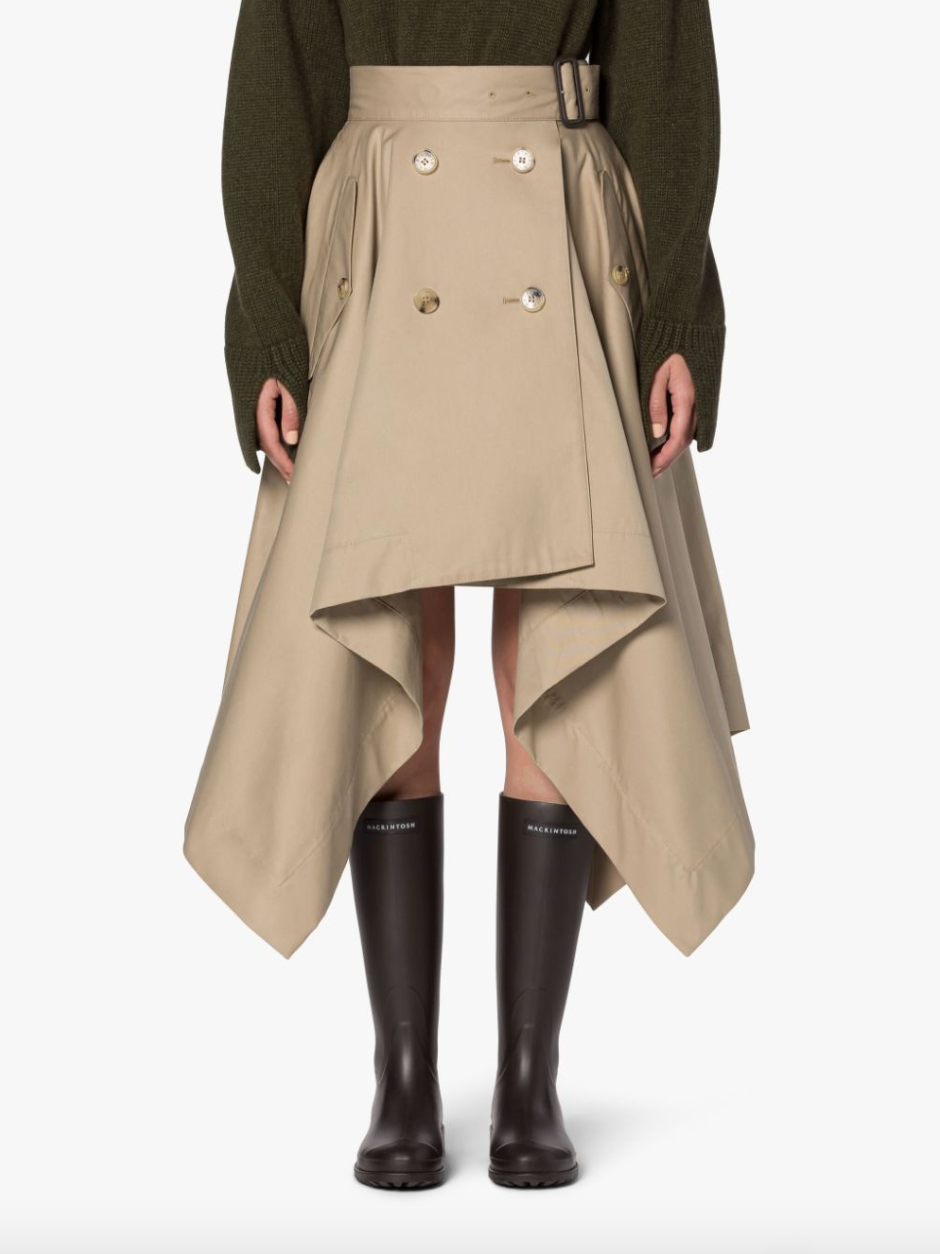 Female model wearing a tan skirt with belted waist, double button detailing and side flap pockets