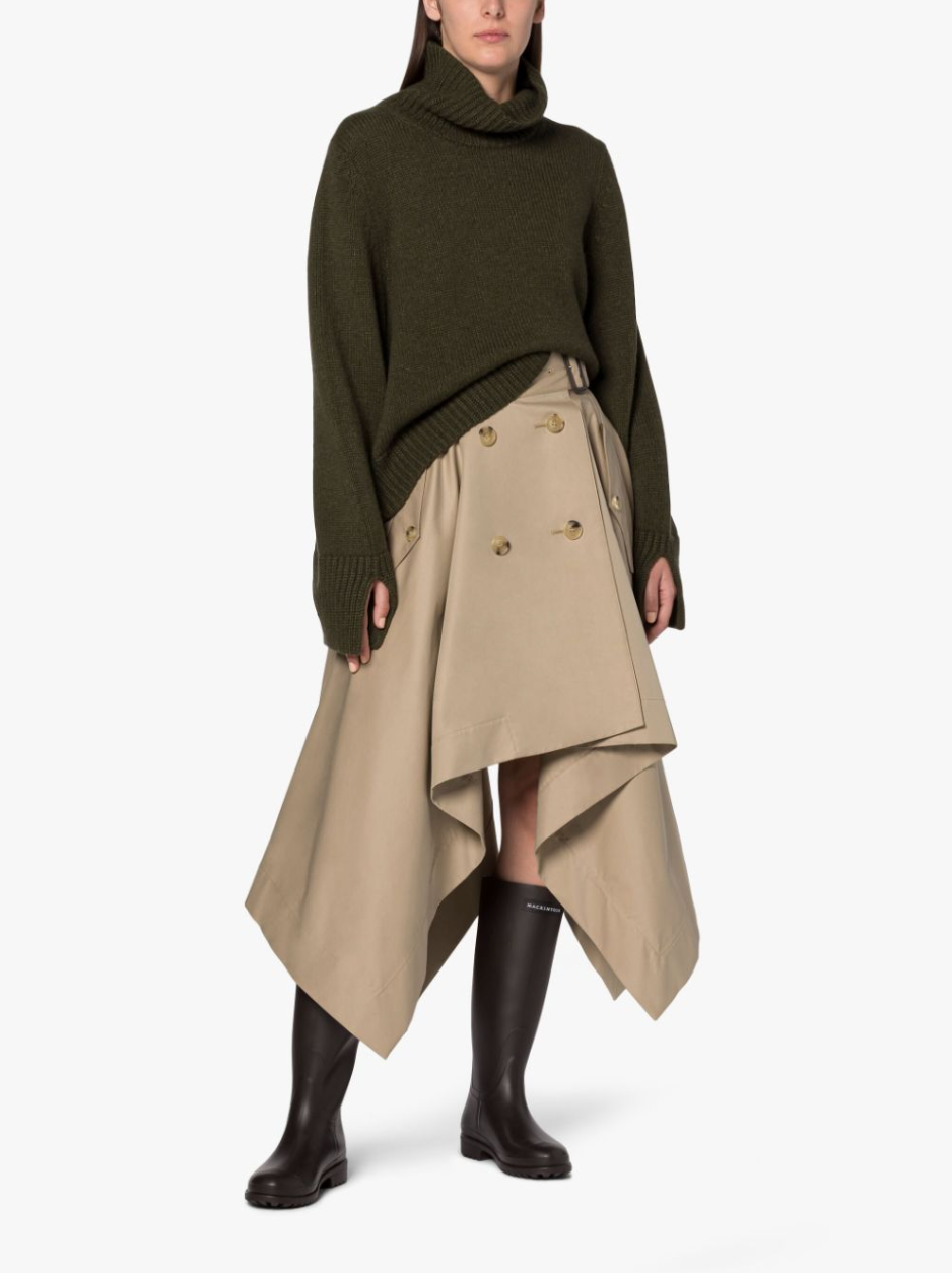 Female model wearing a tan skirt with belted waist, double button detailing and side flap pockets