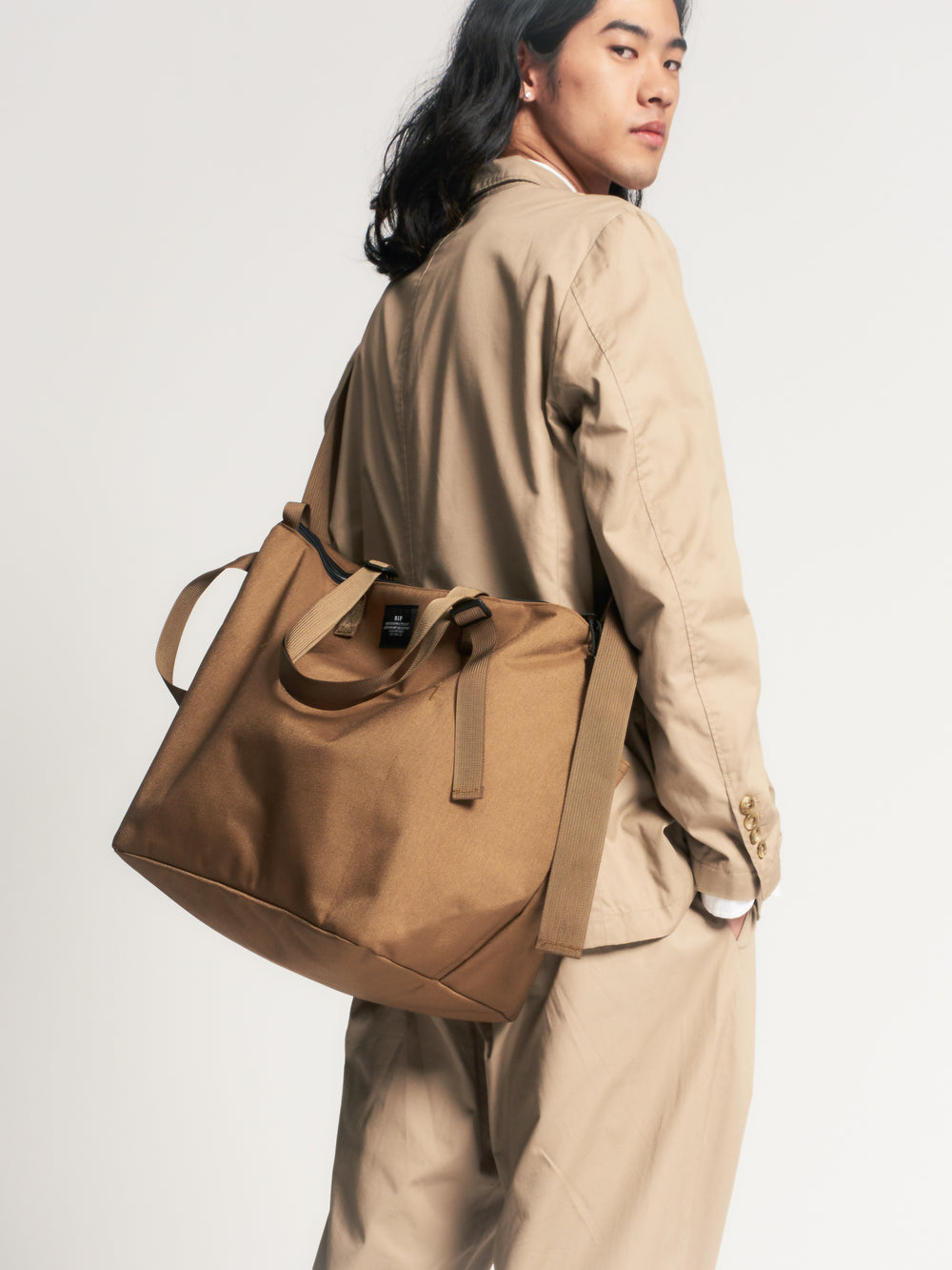 Male model wearing khaki colored canvas tote across his back