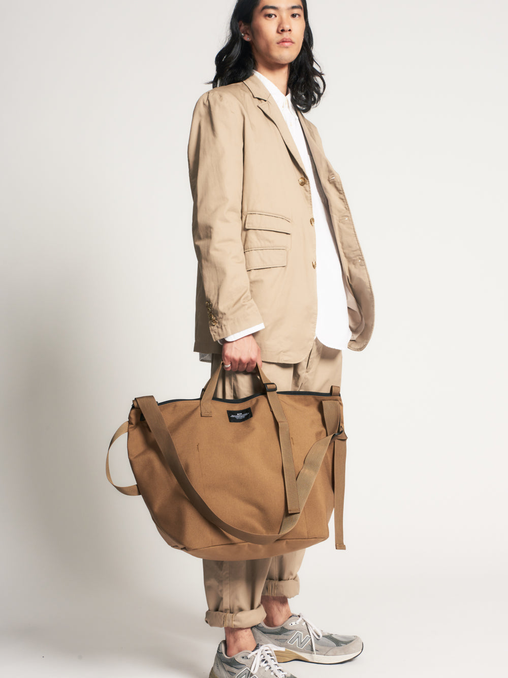Male model holding khaki colored canvas tote by the handle