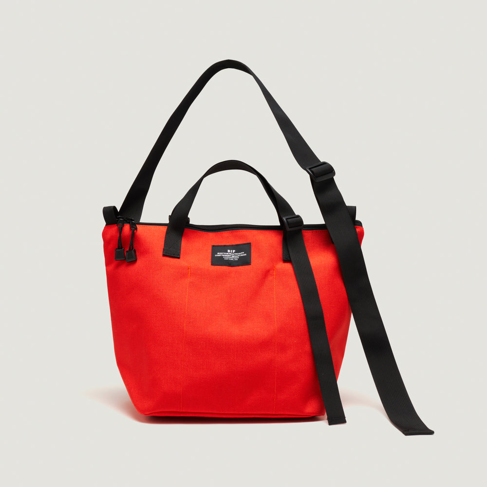 Reddish-orange tote bag with exterior pockets, black handle & shoulder strap, and  zipper closure