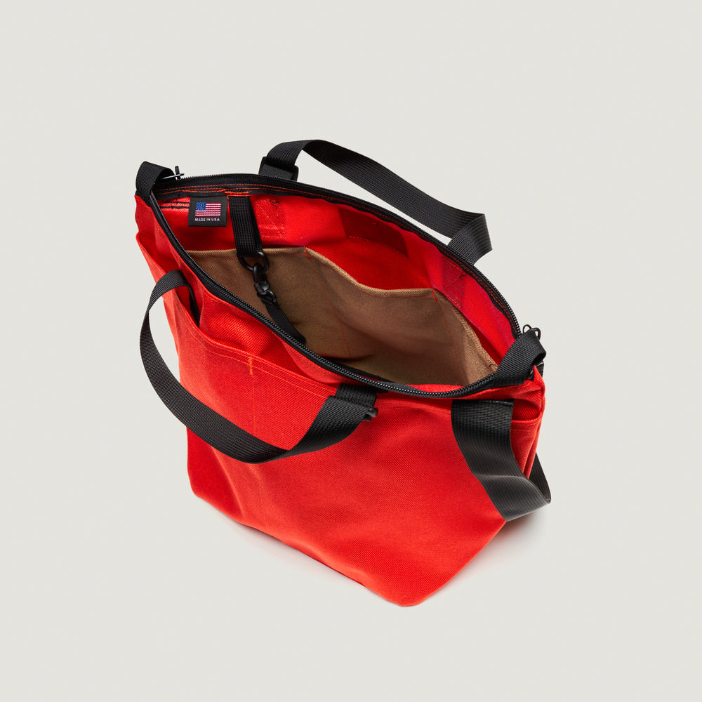 Reddish-orange tote bag with exterior pockets, black handle & shoulder strap, and  zipper closure (interior view)
