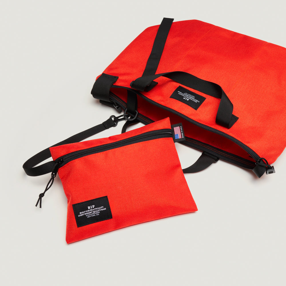 Reddish-orange tote bag with black handle & shoulder strap, zipper closure, and detachable interior zip pouch