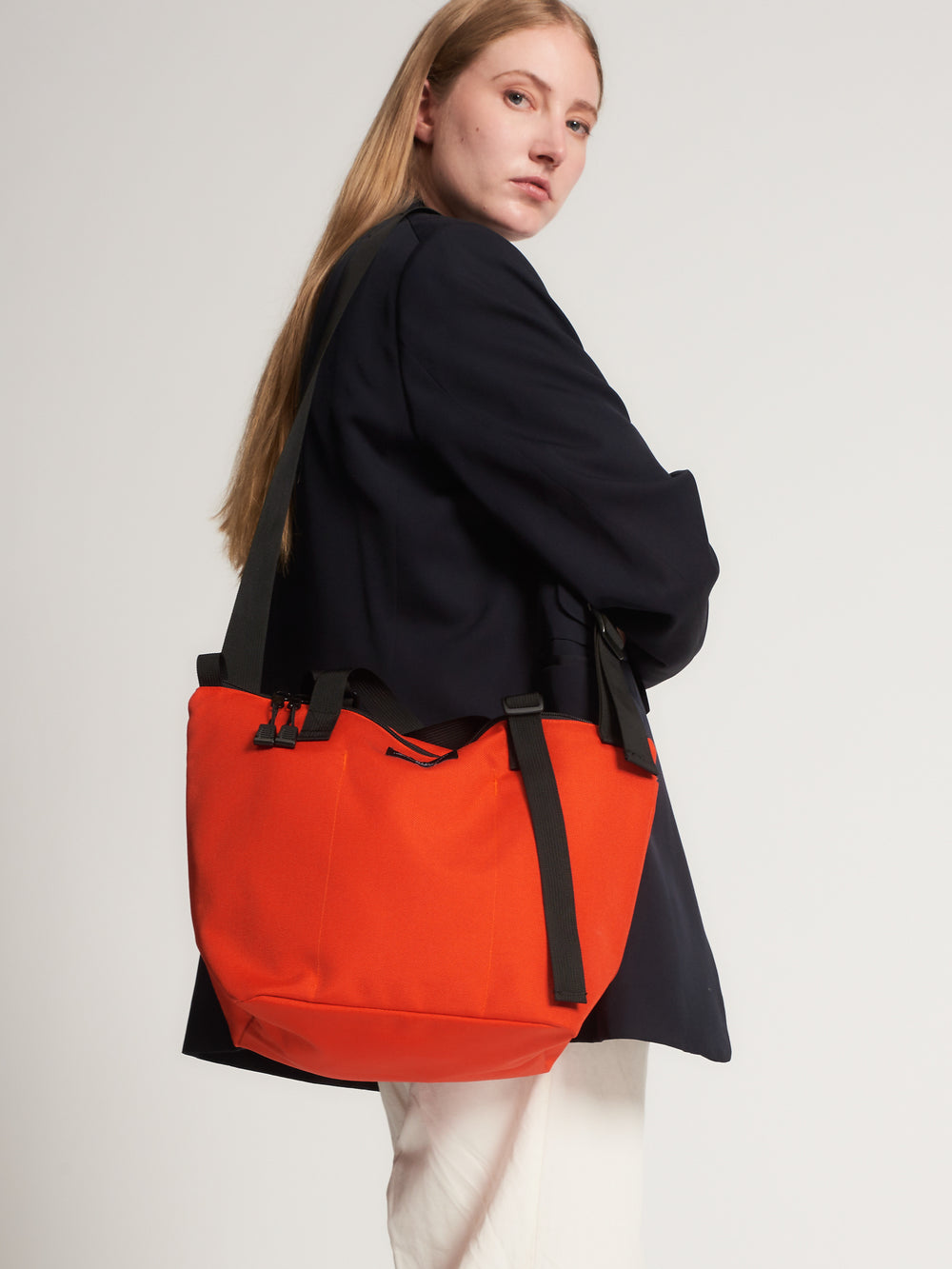Female model carrying reddish-orange tote bag with black shoulder strap