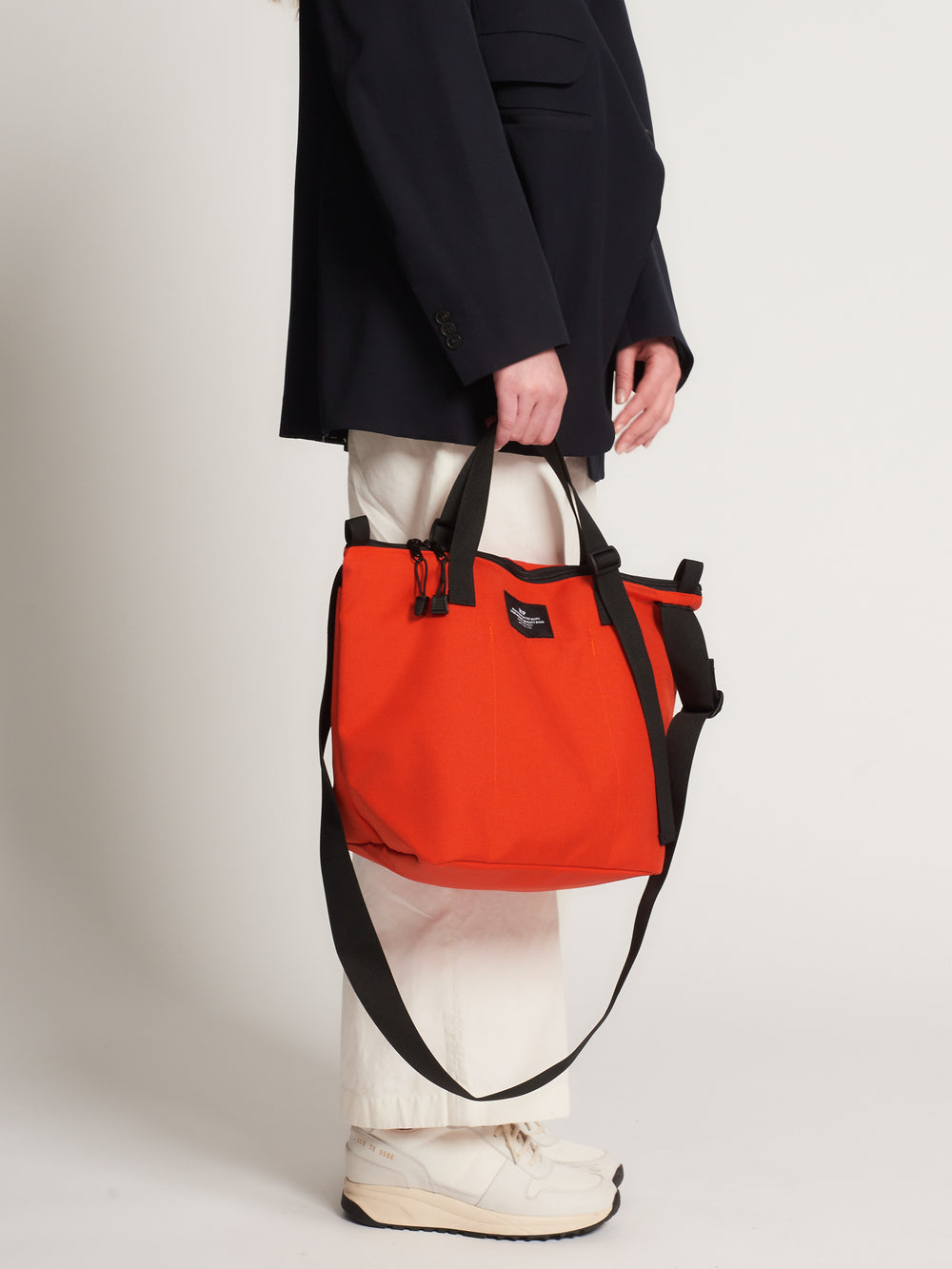 Model carrying reddish-orange tote bag with black handle