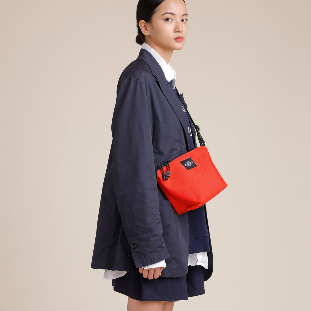 Female model wearing reddish-orange nylon canvas bag in crossbody manner