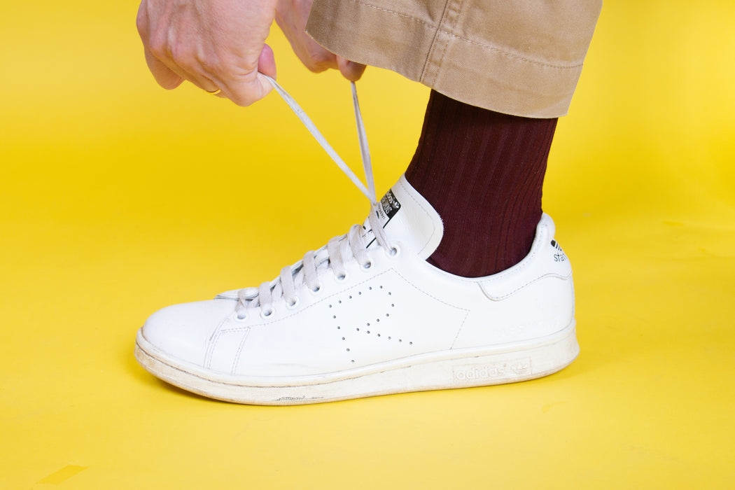 Man wearing burgundy socks in white sneakers tying his shoelaces