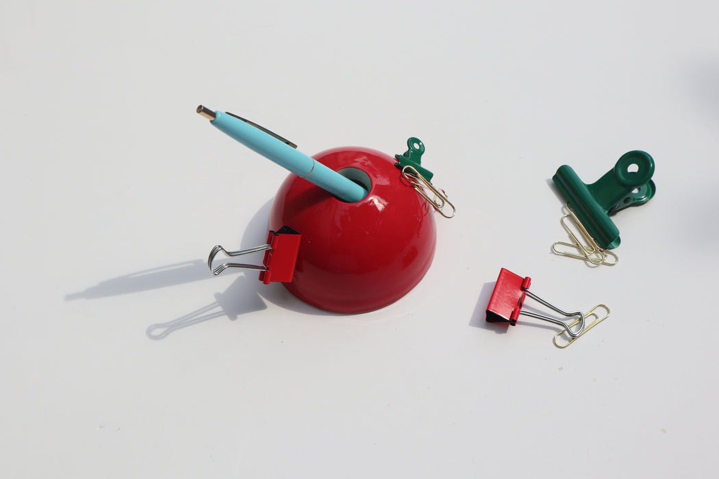 Red Hemisphere Magnetic Ceramic Paperweight with blue pen inside and metal clips scattered around it