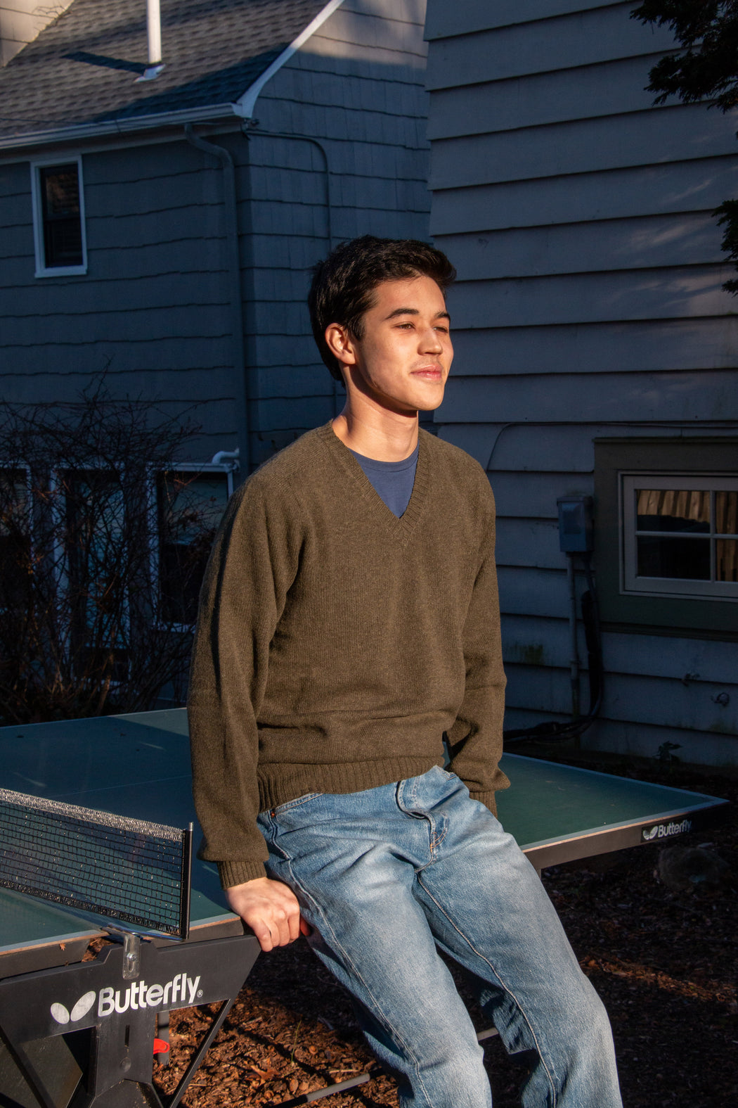 Male model wearing dark olive green long sleeve V-neck sweater & jeans