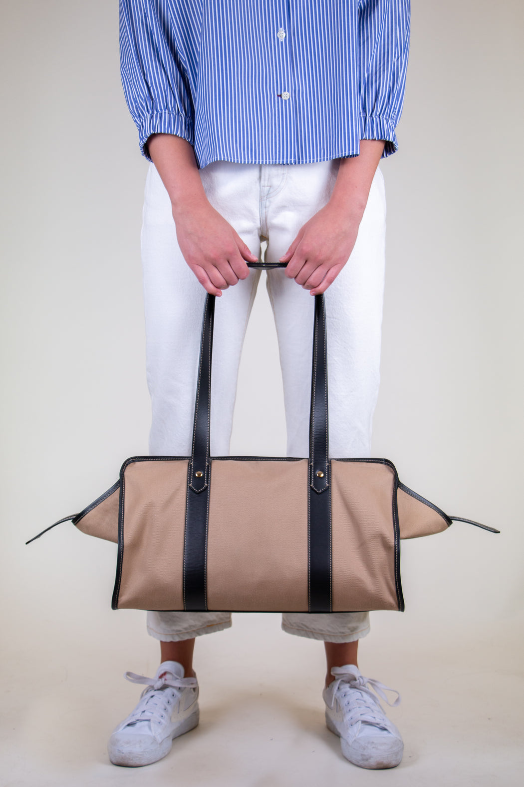 Model holding tan cotton twill weekender bag with leather handles