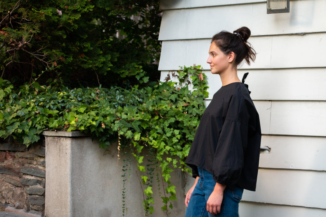 Girl wearing black popover shirt with grosgrain ribbon tie back closure with dropped sleeves and puffy sleeves.