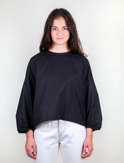 Girl wearing black popover shirt with grosgrain ribbon tie back closure with dropped sleeves and puffy sleeves.