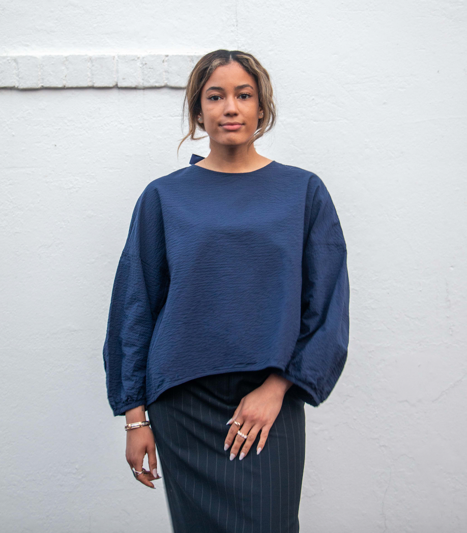 Model wearing dark blue popover shirt with long sleeves and grosgrain ribbon tie back closure and striped crinkle