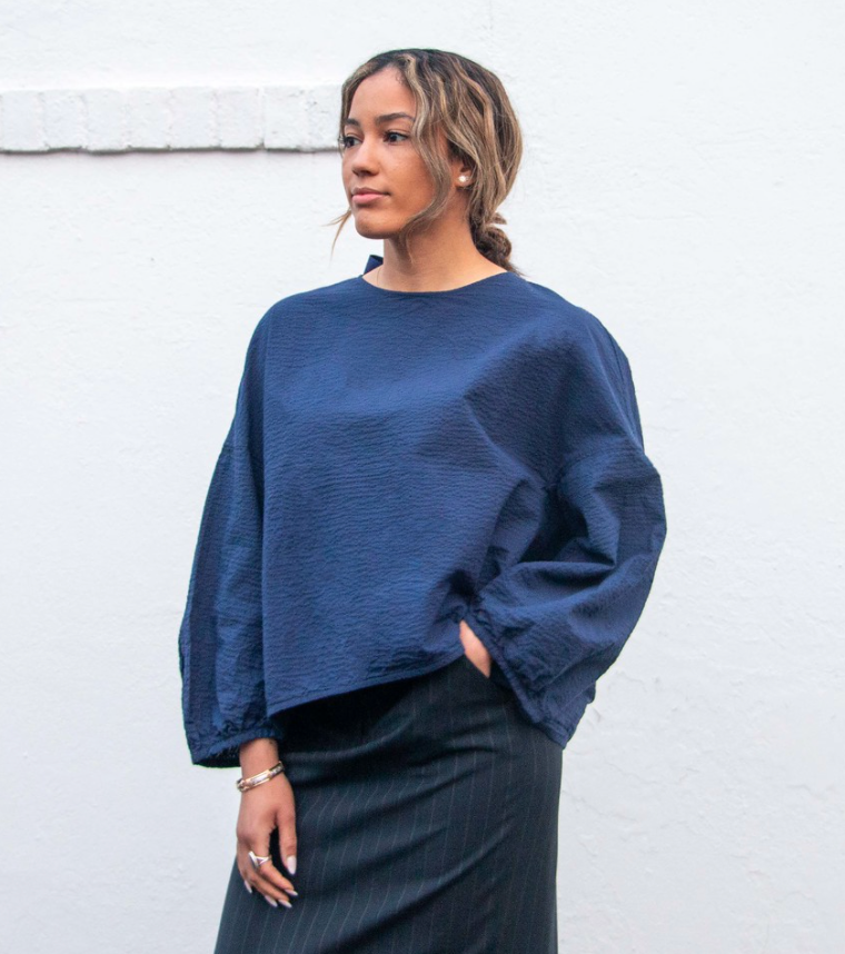 Model wearing dark blue popover shirt with long sleeves and grosgrain ribbon tie back closure and striped crinkle