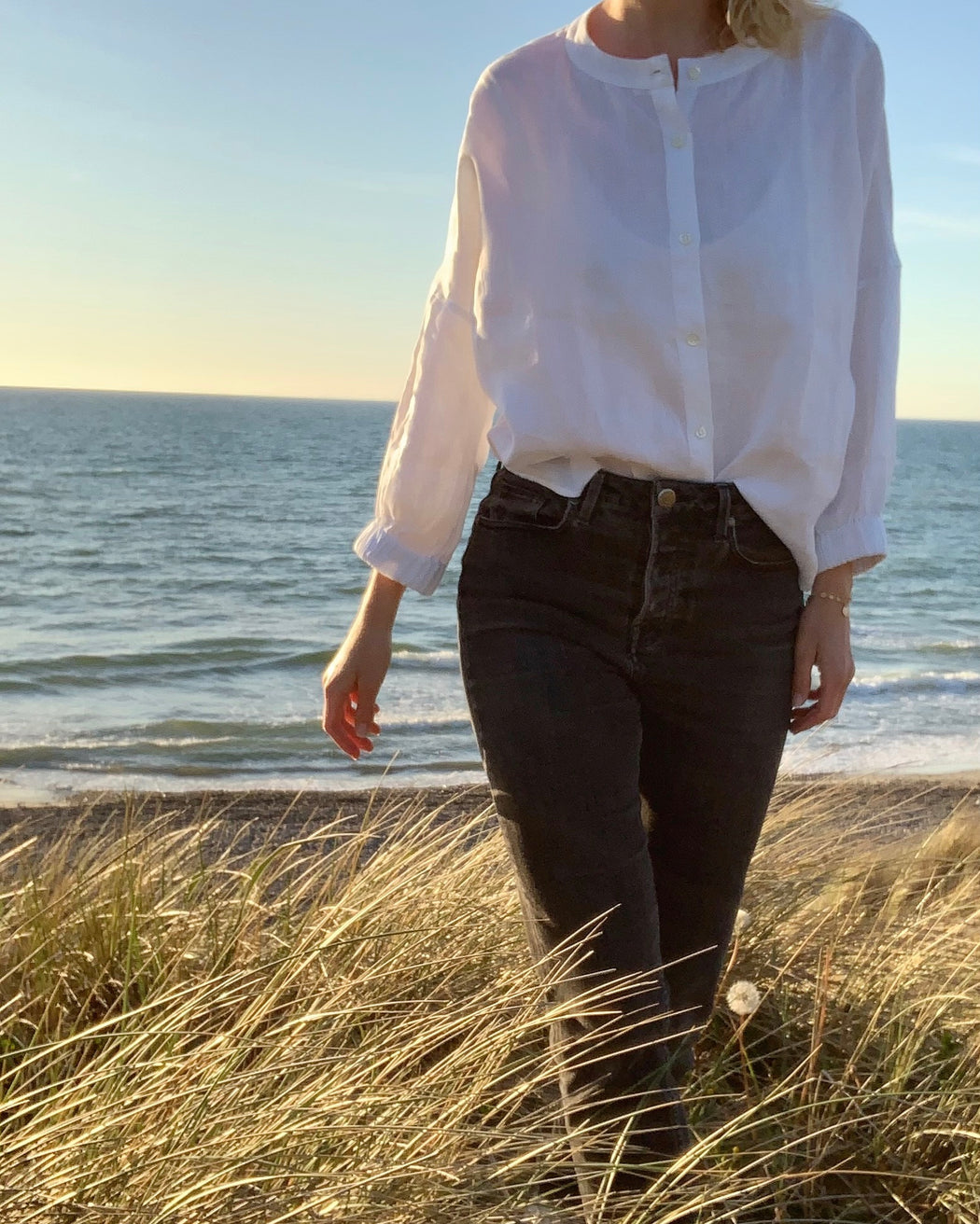 Model wearing white button down shirt with long sleeves and curved collar, and jeans