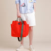 Male model holding a large reddish-orange tote bag with exterior pockets and olive green handles and strap