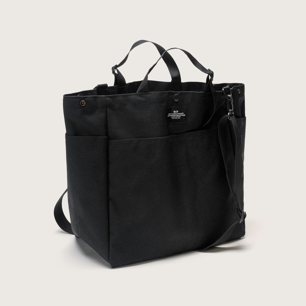 Black tote bag with snap closure, exterior pockets, top handles & shoulder strap (front view)