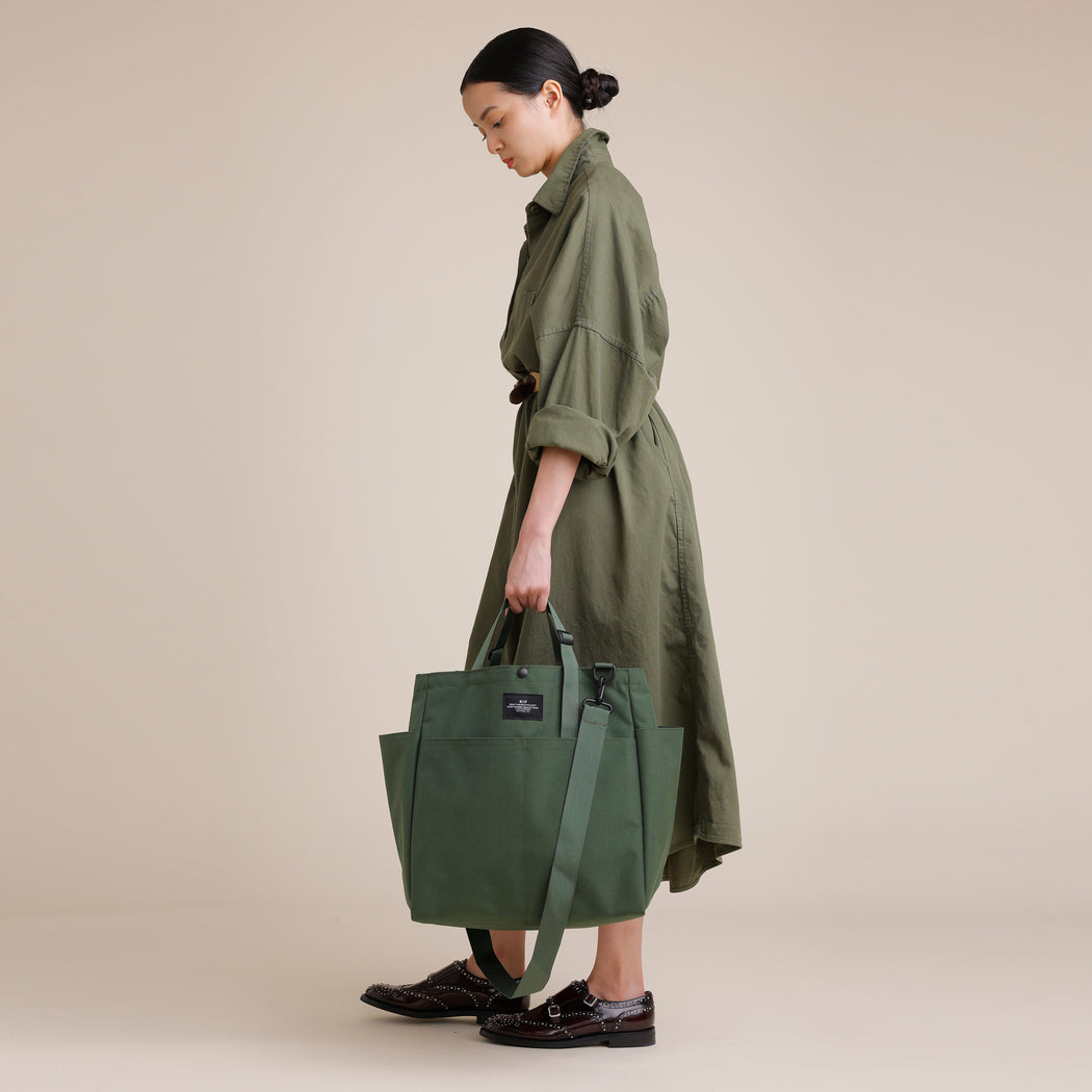 Female model holding olive green colored canvas tote bag by the handles 