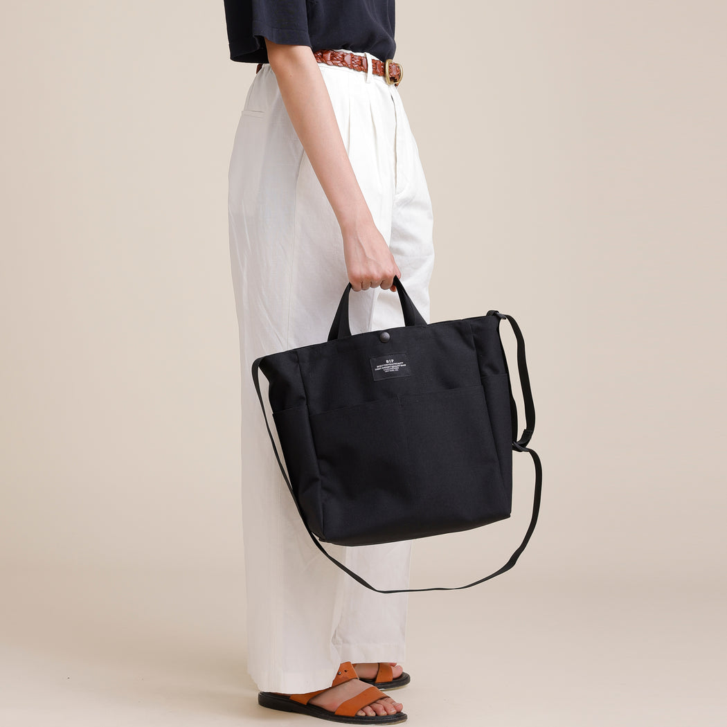 Female model holding black canvas tote with handles & shoulder strap