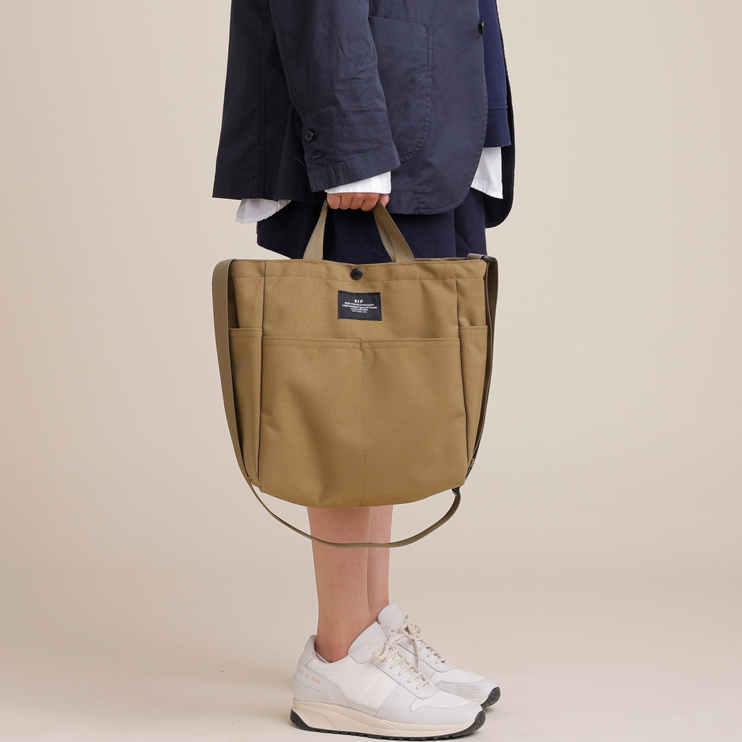 Female model carrying khaki colored canvas tote by the handles