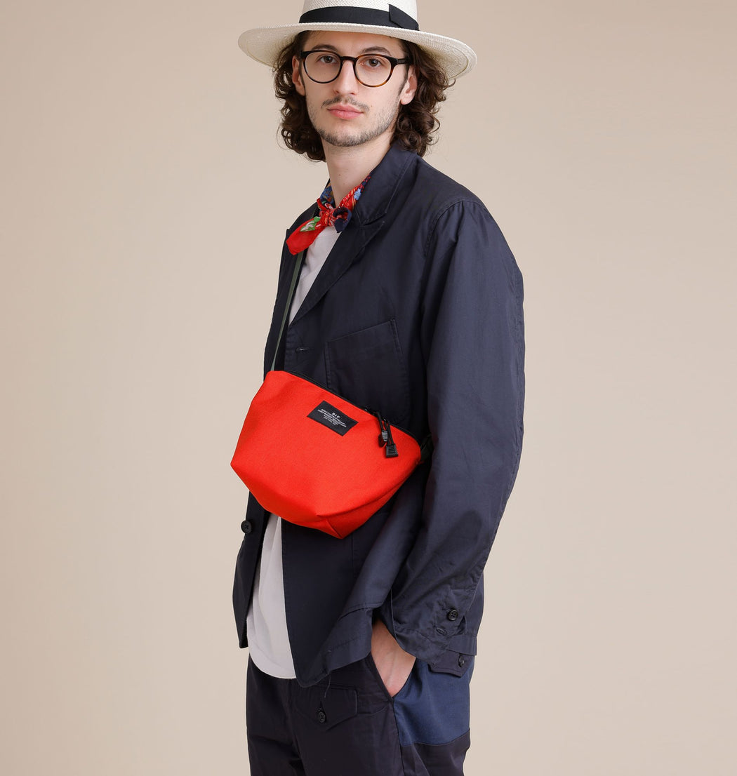 Male model wearing reddish-orange nylon canvas bag in crossbody manner