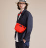 Male model wearing reddish-orange nylon canvas bag in crossbody manner