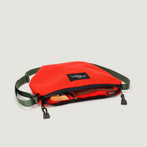 Small reddish-orange nylon canvas bag with zip closure & olive green adjustable shoulder strap & interior pockets