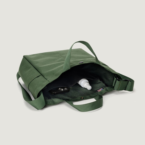 Olive green colored canvas tote lying on it's side showing 2 internal pockets, top handles & shoulder strap