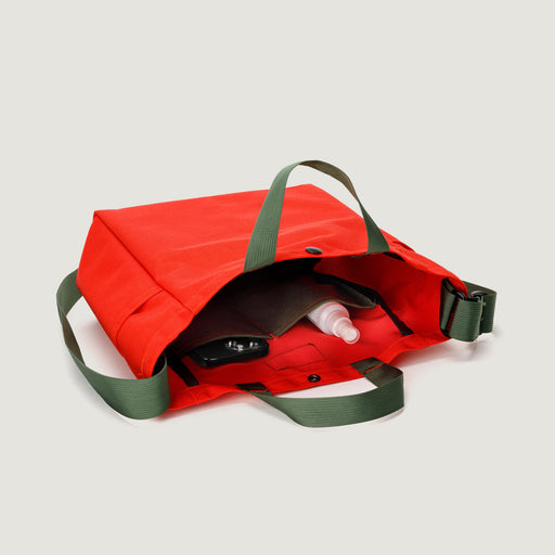 Reddish-orange tote bag  lying on it's side, showing interior organization pockets + handles and shoulder strap in olive green color