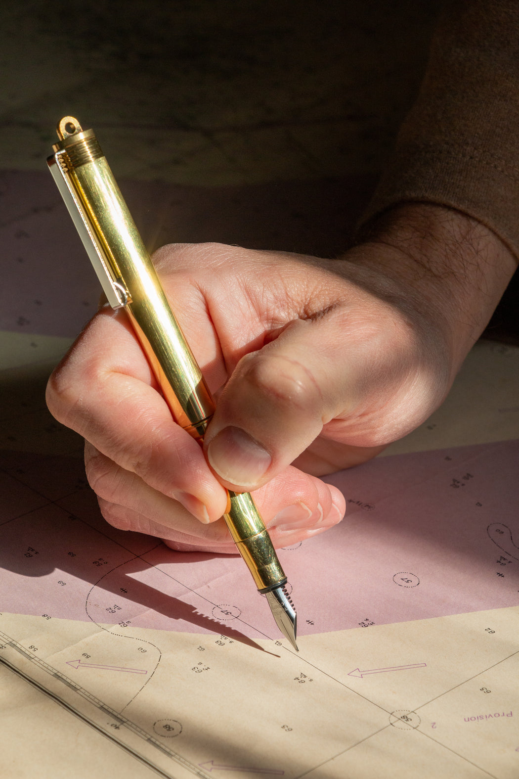 Man using brass fountain pen writing on map