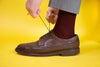 Man wearing burgundy socks in brown leather shoes tying his shoelaces