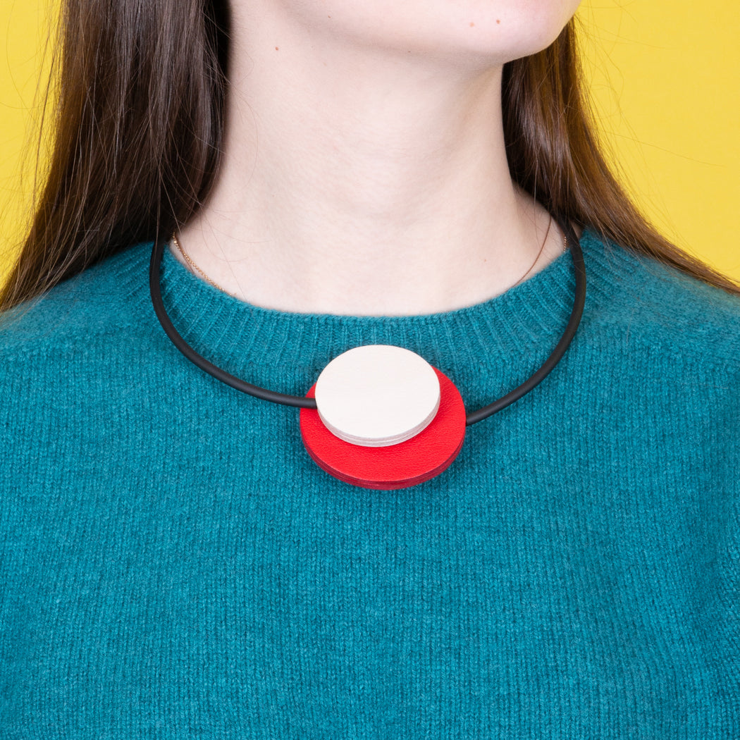 Model wearing a black band choker necklace with red & white leather circles on top of a blue sweater