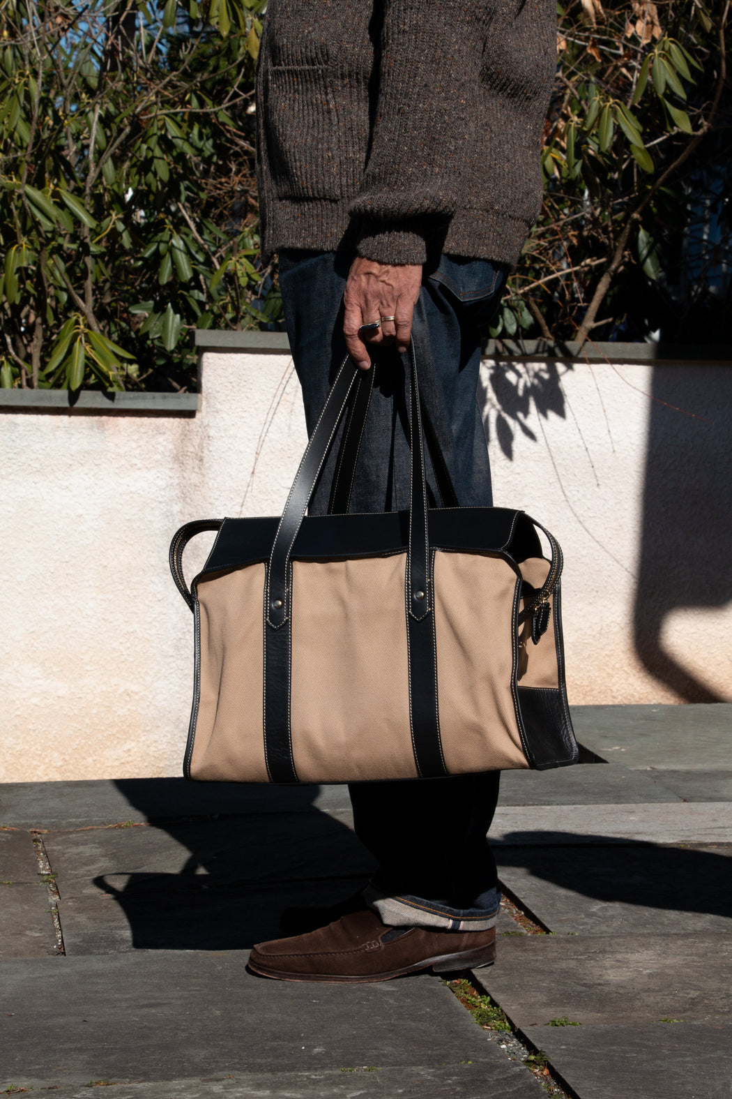 Model holding tan cotton twill weekender bag with leather handles
