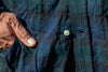 Close-up of mother of pearl button  and button hole on blue & green plaid crinkle shirt