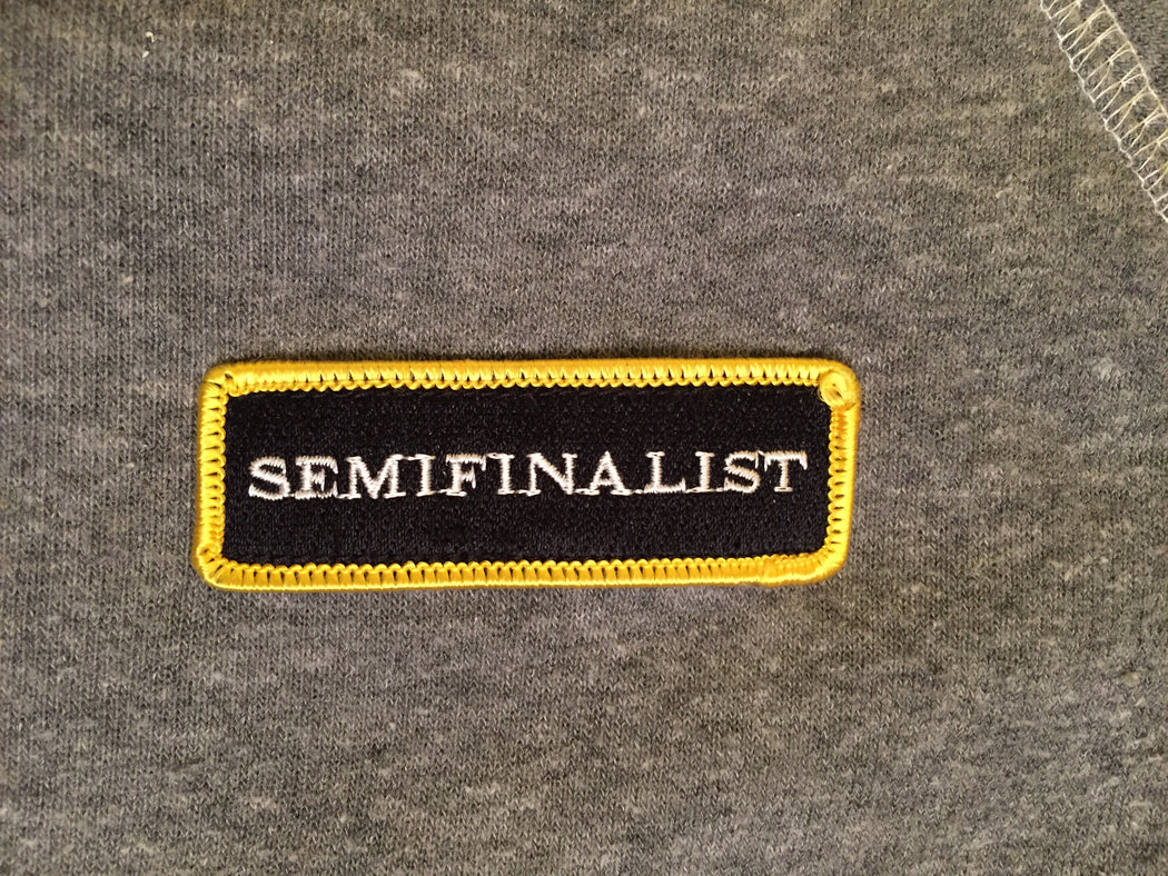 Close-up on SEMIFINALIST logo appliqué: black with white logo & yellow trim