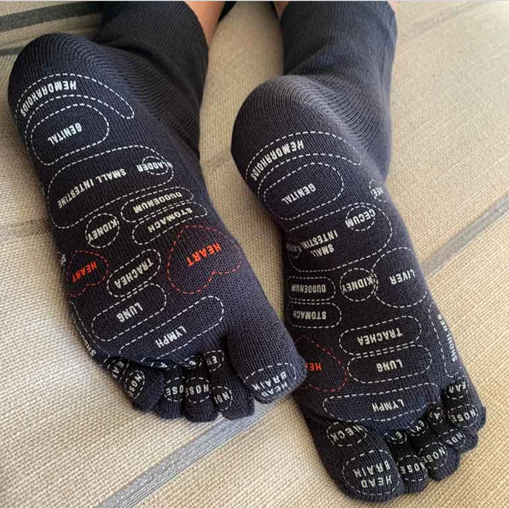 Model wearing dark grey toe socks with reflexology points mapped out on bottom