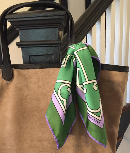 Green & white geometric silk square scarf with purple trim, tied to a tan suede tote