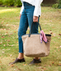 Model carrying tan suede tote with black leather trim and handles, with red & white scarf tied on one handle