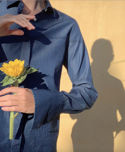 Woman wearing denim blue long sleeve tuxedo shirt, holding a flower