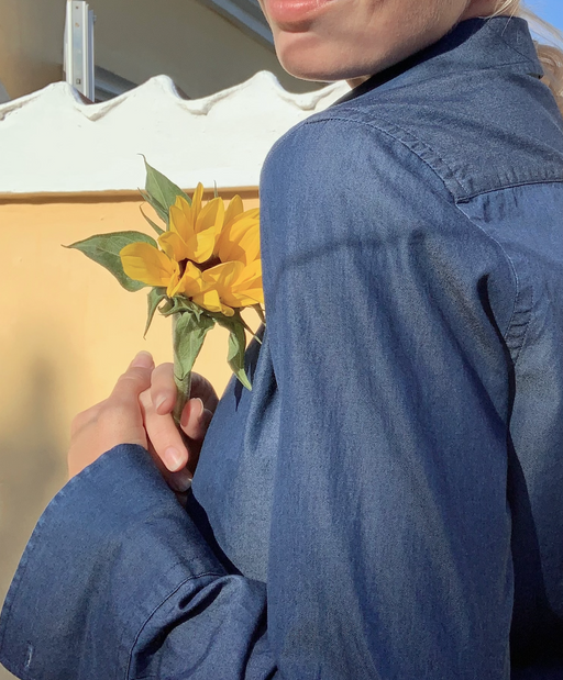 Woman wearing denim blue long sleeve tuxedo shirt, holding a flower