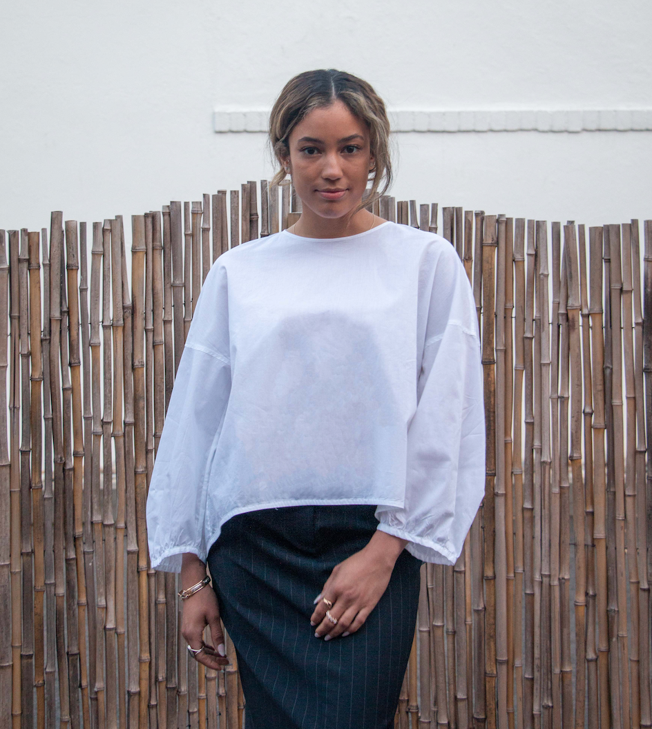 Female model wearing a white semi-sheer popover shirt with puffy long sleeves and rounded neck and hemline