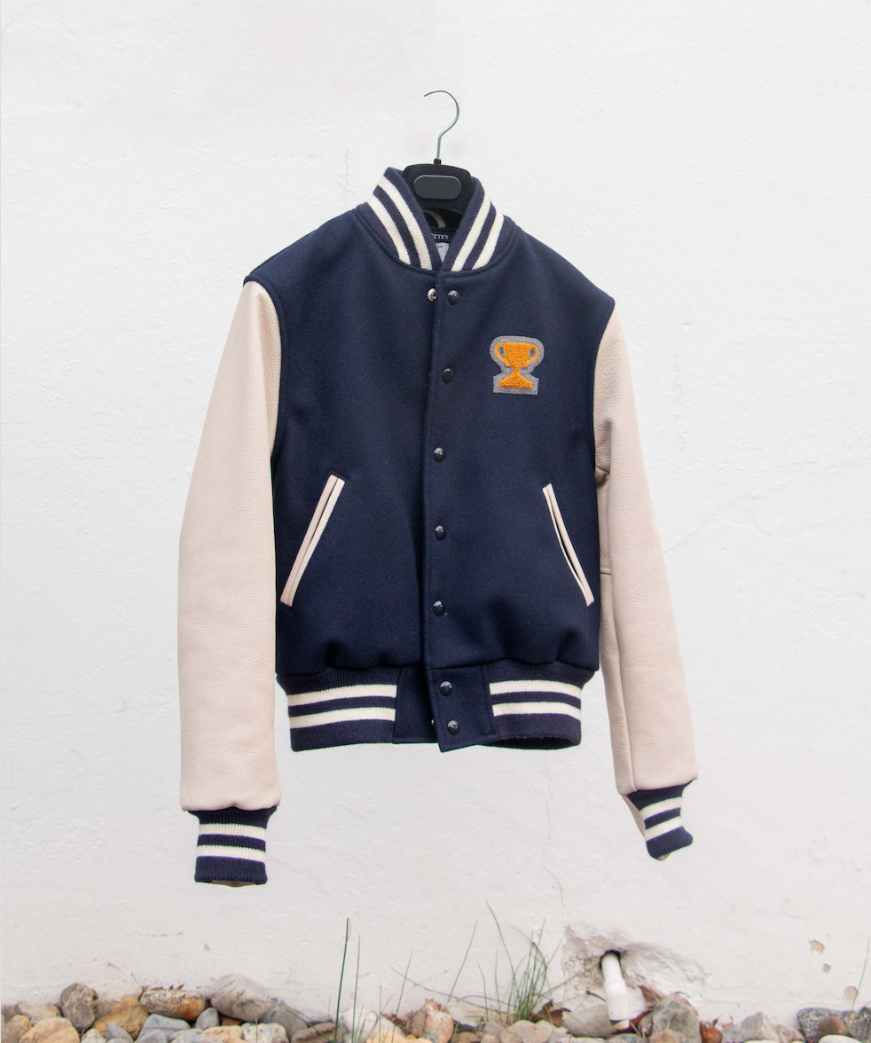 navy blue varsity jacket with white leather sleeves and  trophy logo patch