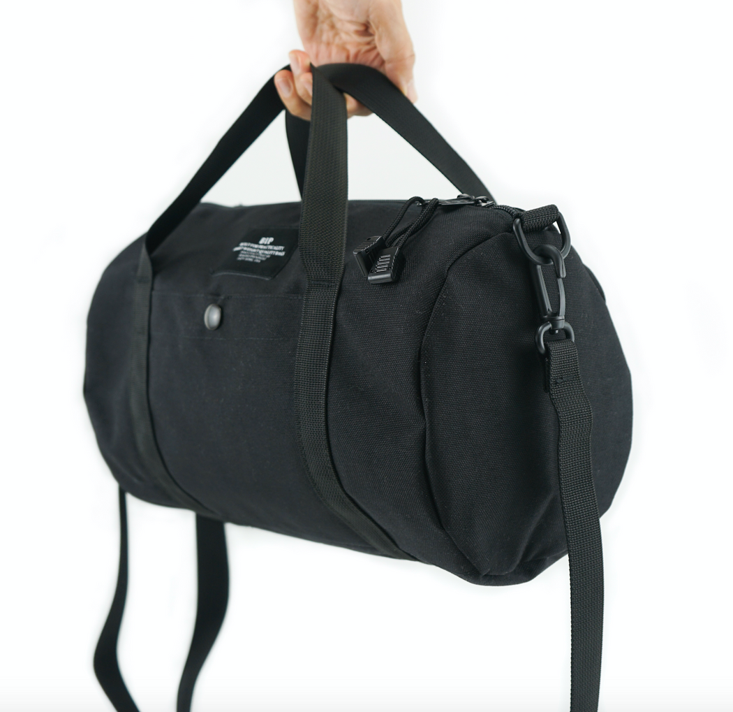 Hand held black canvas duffle bag with front pocket, handles and removable shoulder straps